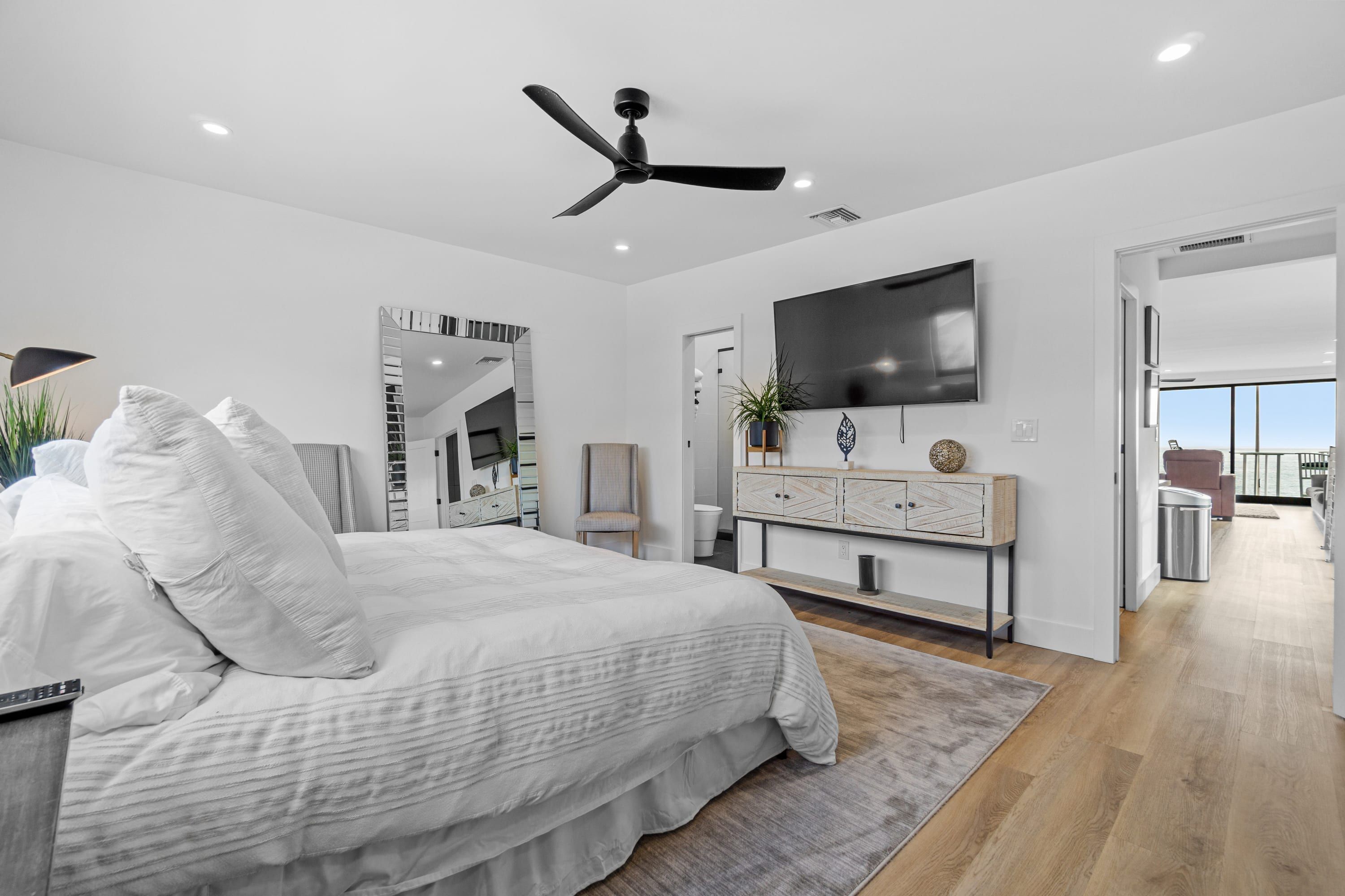 Une chambre à coucher moderne avec un grand lit, un ventilateur de plafond, une télévision et une vue sur l’extérieur.