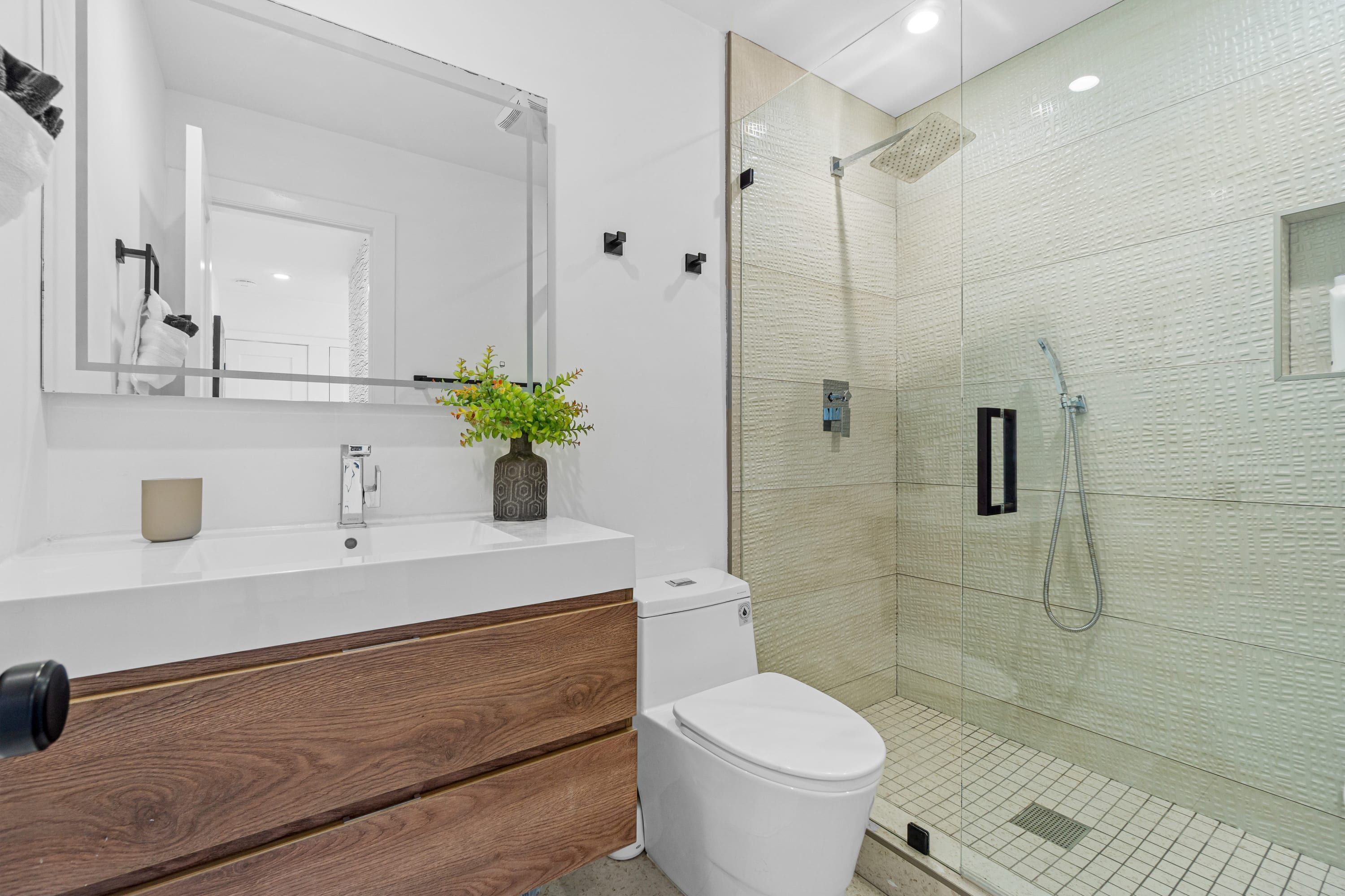 A modern bathroom with a white vanity, wooden drawer, white toilet, and a glass shower enclosure.