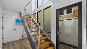 Una escalera moderna con escalones de madera y barandillas metálicas, que conduce a una puerta de cristal con vistas a un tejado de tejas.