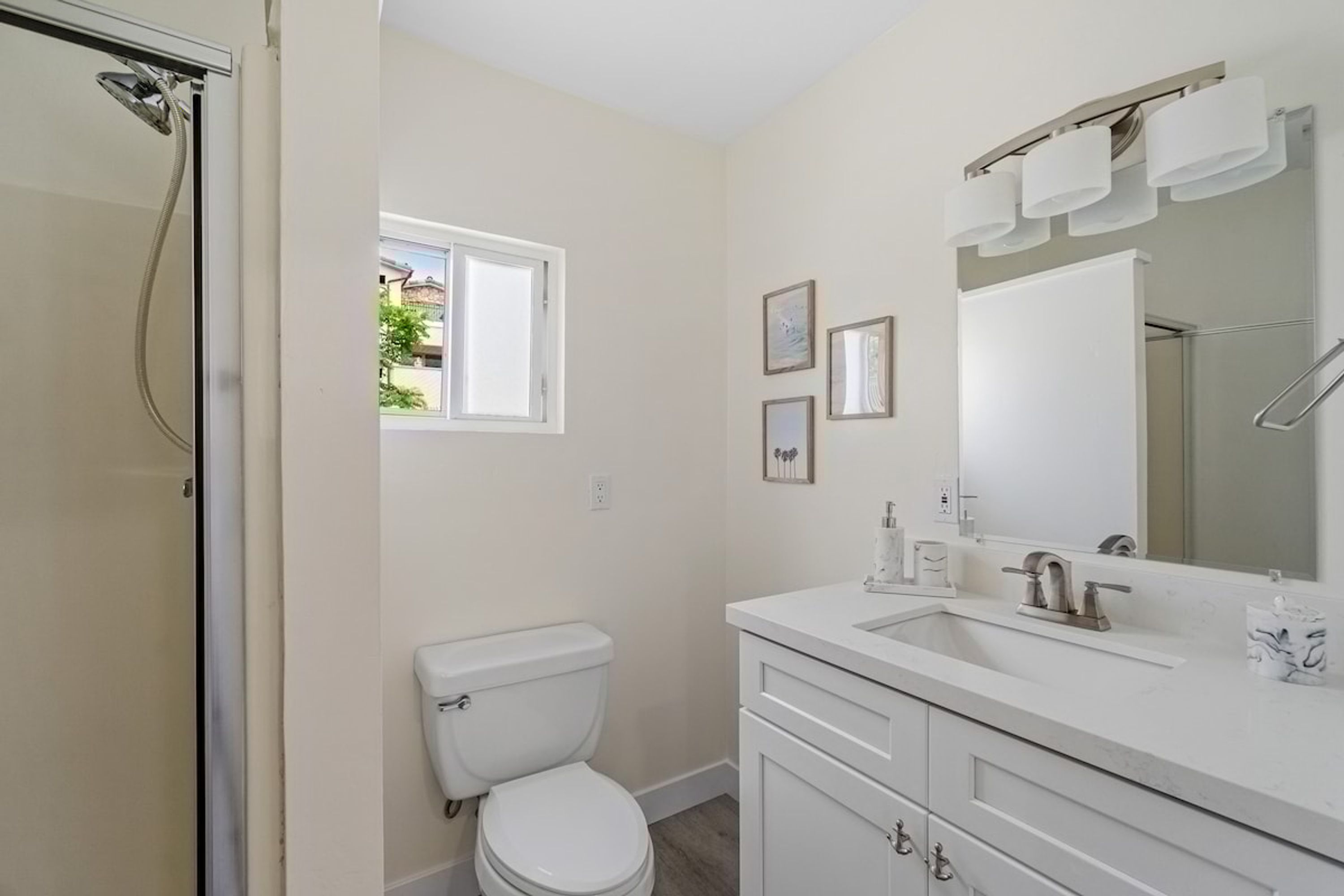 A bathroom with a toilet, sink, and shower. There is a window providing natural light and a mirror above the sink.