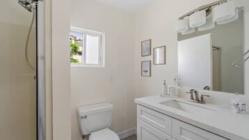 A bathroom with a toilet, sink, and shower. There is a window providing natural light and a mirror above the sink.