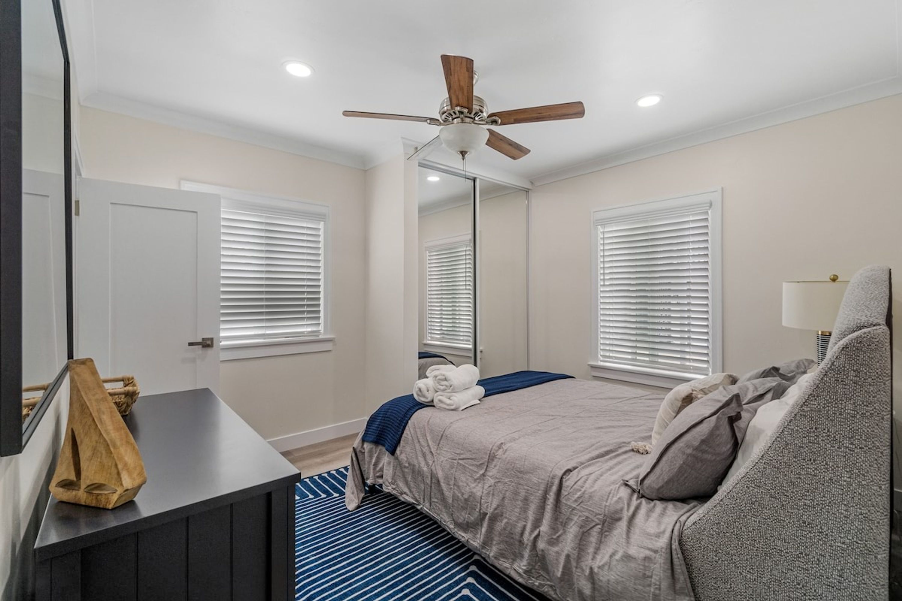 A bedroom with a bed, a ceiling fan, a bedside table, and a window with blinds.