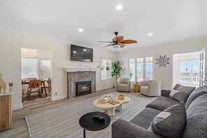 A living room with a fireplace, a large sofa, a coffee table, and a TV mounted on the wall. - Carlsbad Blvd Villa in Carlsbad (Carlsbad)