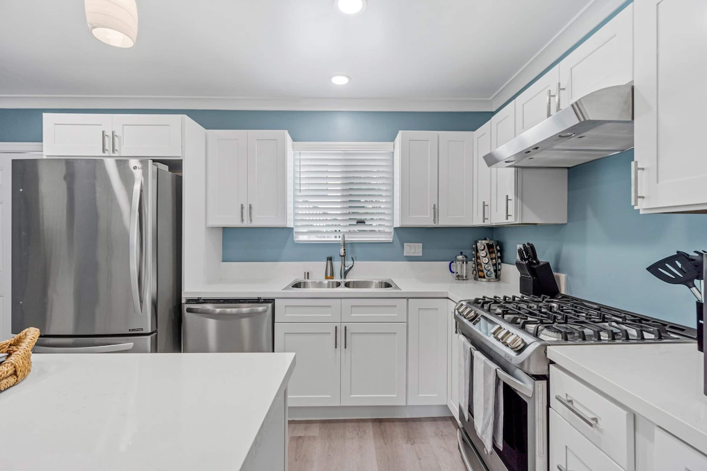 A modern kitchen with white cabinets, stainless steel appliances, and a blue accent wall.