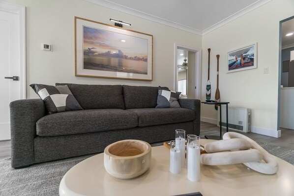 A living room with a grey sofa, a wooden bowl, candles, and framed artwork on the walls. - Carlsbad Blvd Villa in Carlsbad (Carlsbad)