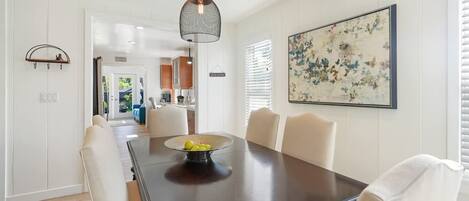 A dining area with a dark wooden table, white chairs, and a hanging pendant light.