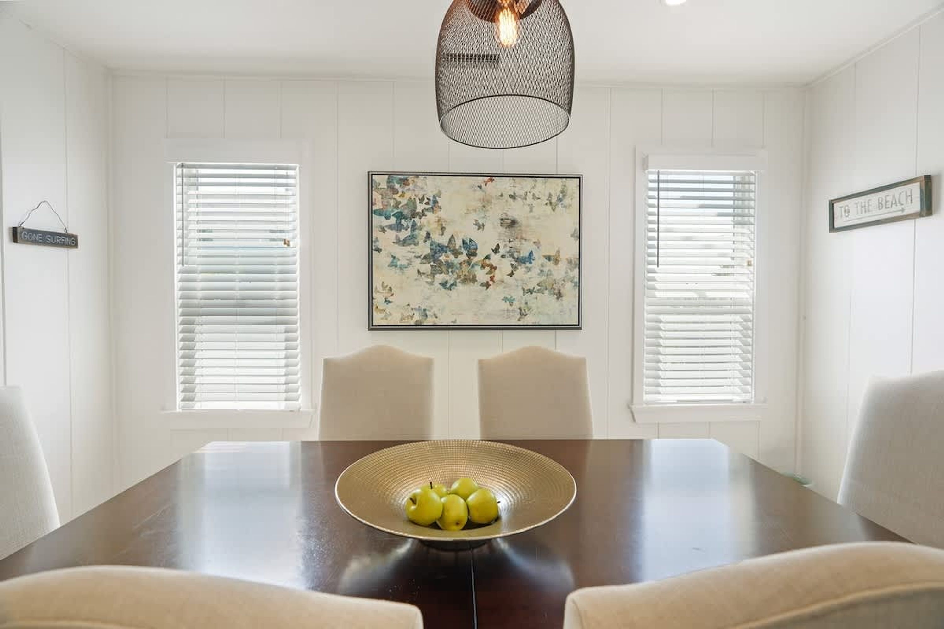 A dining room with a wooden table, two chairs, a bowl of fruit, and a pendant light.