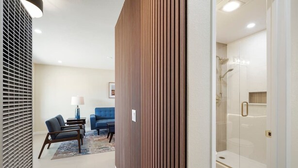 A modern hotel room with a glass shower, a seating area with a blue sofa and chairs, and a wooden accent wall. - Urban Oasis - Just Remodeled (San Diego)