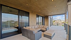 A modern balcony with a sofa and ottoman, large windows, and a view of buildings. - Dana Point Luxe Str14-007 (Dana Point)