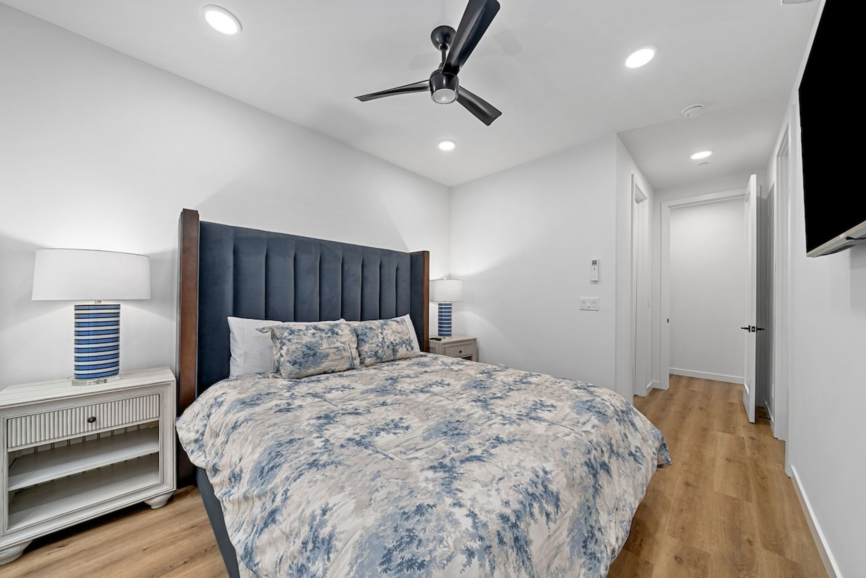 A bedroom with a bed, nightstands, a ceiling fan, and a TV mounted on the wall.