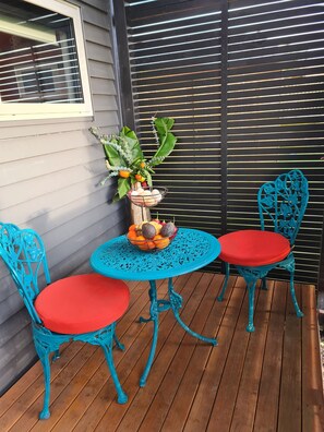 Une terrasse en bois avec une table bleue et deux chaises turquoise dotées de coussins rouges.