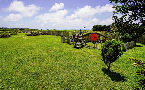 A well-maintained grassy area with a wooden fence, a small wooden structure with a red door, and a tree in the foreground.