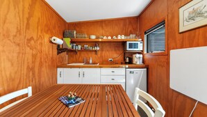 A compact kitchen with wooden walls, a white refrigerator, a microwave, and a sink.