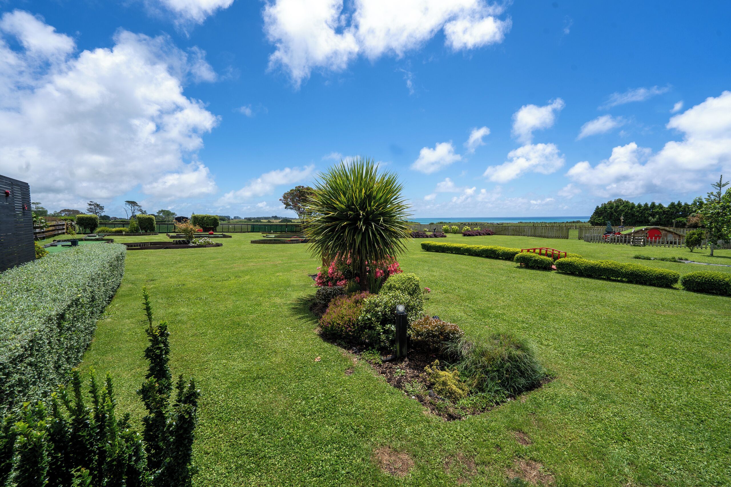 A well-maintained garden with manicured lawns, a variety of shrubs, and a prominent palm tree.