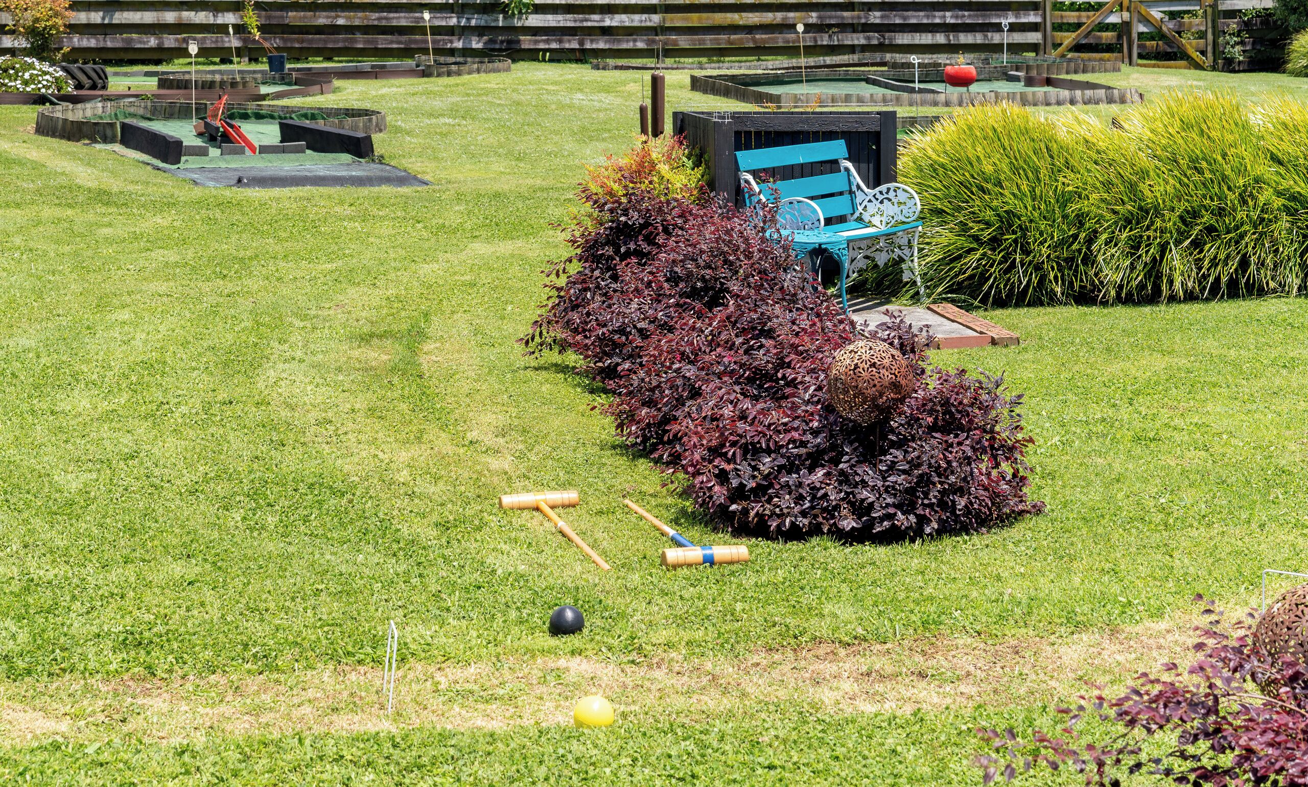 Une pelouse bien entretenue, avec des équipements de croquet, un banc et une haie.