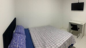 Una habitación pequeña y poco amoblada, con una cama, un escritorio y un televisor montado en la pared.