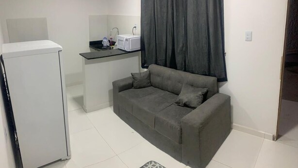 Un espacio habitable pequeño con kitchenette, un sofá gris y un refrigerador blanco.