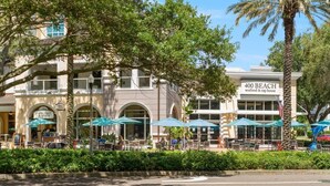 A beachfront restaurant with outdoor seating and palm trees.