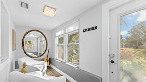 A hallway with a white chair, a guitar, and a mirror.