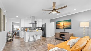 A modern living space with a kitchen, dining area, and a large window with a sunset view.