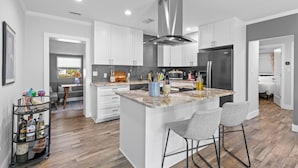 A modern kitchen with white cabinetry, a central island with bar stools, and a stainless steel range hood.