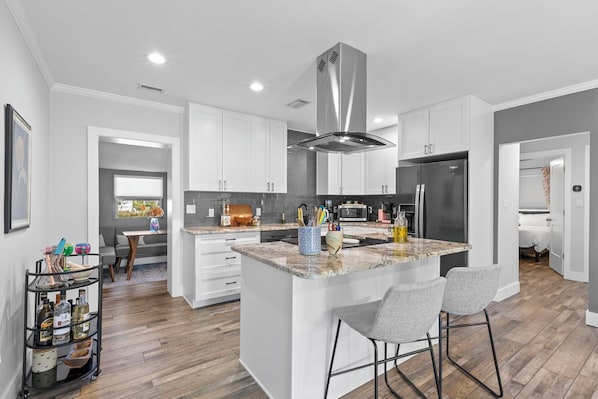 A modern kitchen with white cabinetry, a central island with bar stools, and a stainless steel range hood.