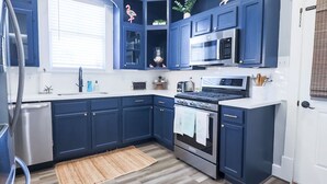 A modern kitchen with dark blue cabinets, a stainless steel refrigerator, a microwave, and a stove. - Vibrant Bungalow 2 Minutes to the Beach (Galveston)