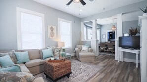 A living room with a sofa, ottoman, and a TV stand. - Vibrant Bungalow 2 Minutes to the Beach (Galveston)