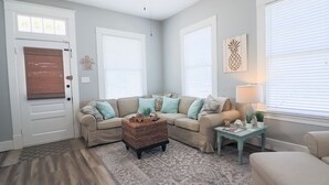A living room with a beige sectional sofa, a wicker coffee table, and a patterned rug. - Vibrant Bungalow 2 Minutes to the Beach (Galveston)