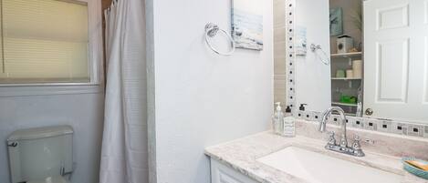 Een badkamer met toilet, douchegordijn, wastafel met spiegel en een plank met toiletartikelen.