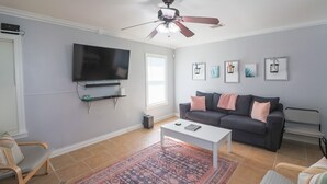 Ein Wohnzimmer mit Flachbildfernseher, Deckenventilator, grauem Sofa, Couchtisch und Teppich mit Muster.