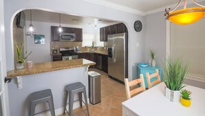 Eine moderne Küche mit Edelstahlkühlschrank, Granit-Arbeitsplatten und hängenden Pendelleuchten.