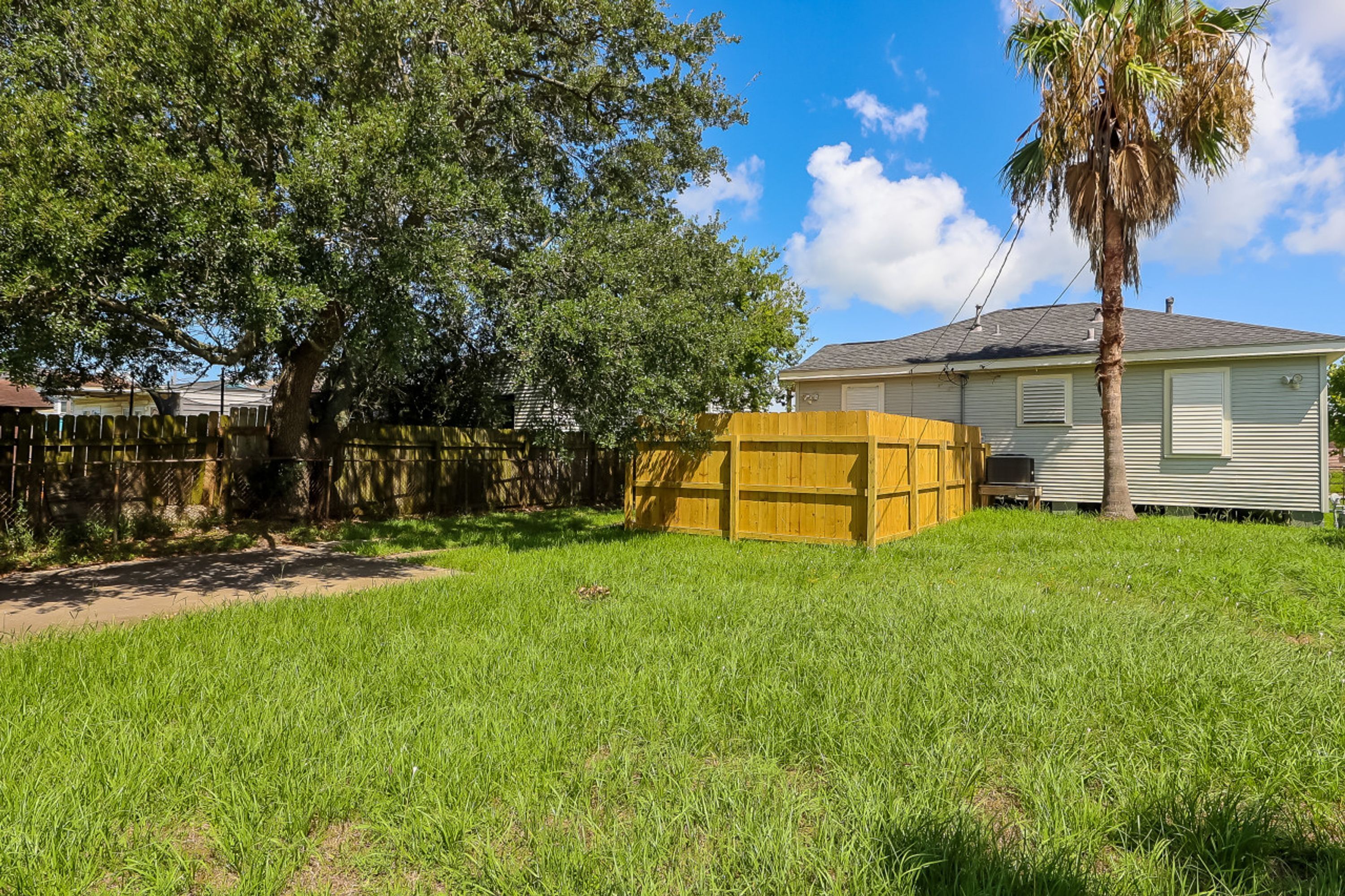 A residential backyard with a wooden play structure, a palm tree, and a house with a grey roof.