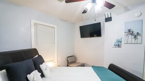 Ein Schlafzimmer mit Bett, Sessel, Fernseher und Deckenventilator.