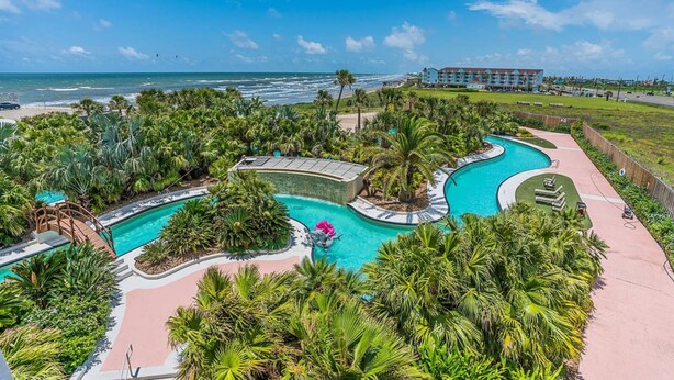 A resort with a large swimming pool, palm trees, and a view of the ocean. - Warm and Welcoming Views at Diamond Beach (Galveston)