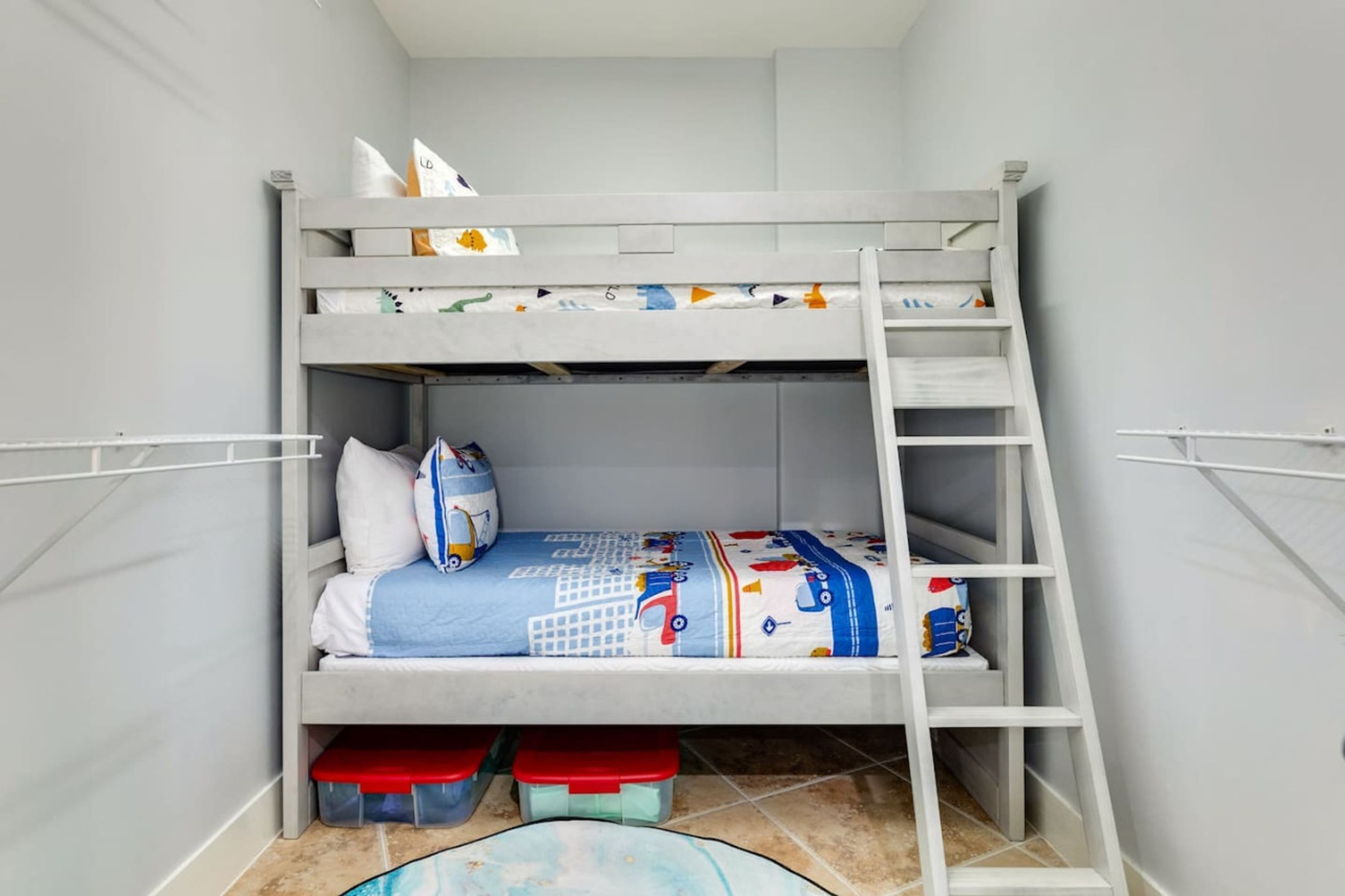 Una cama litera con escalera, cajas de almacenamiento y una colcha estampada.