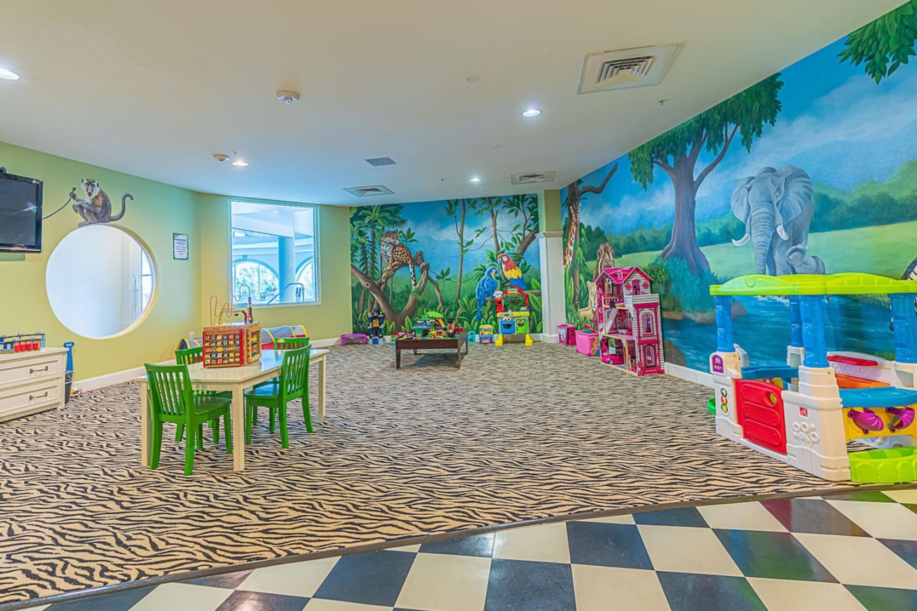 A children's playroom with a zebra-patterned floor, green chairs, a round mirror, and a mural of jungle animals.