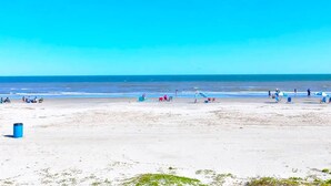 A beach with people, umbrellas, and a clear blue sky. - Beautiful Ocean Views at The Victorian (Galveston)