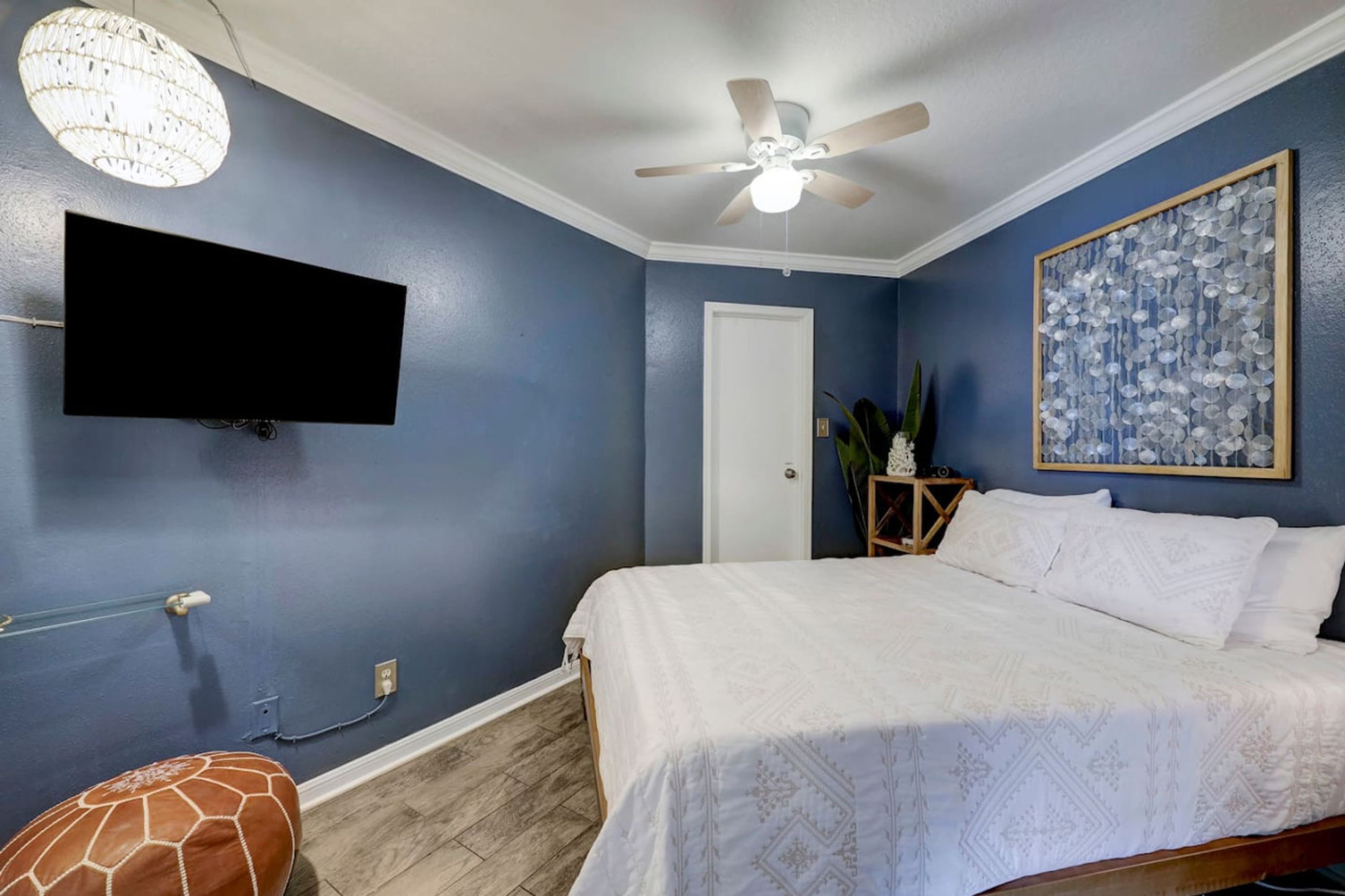 A bedroom with a bed, a ceiling fan, a mounted TV, and a decorative wall piece.
