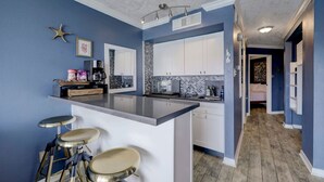A modern kitchen with a bar area, white cabinets, and a blue accent wall. - Beautiful Ocean Views at The Victorian (Galveston)