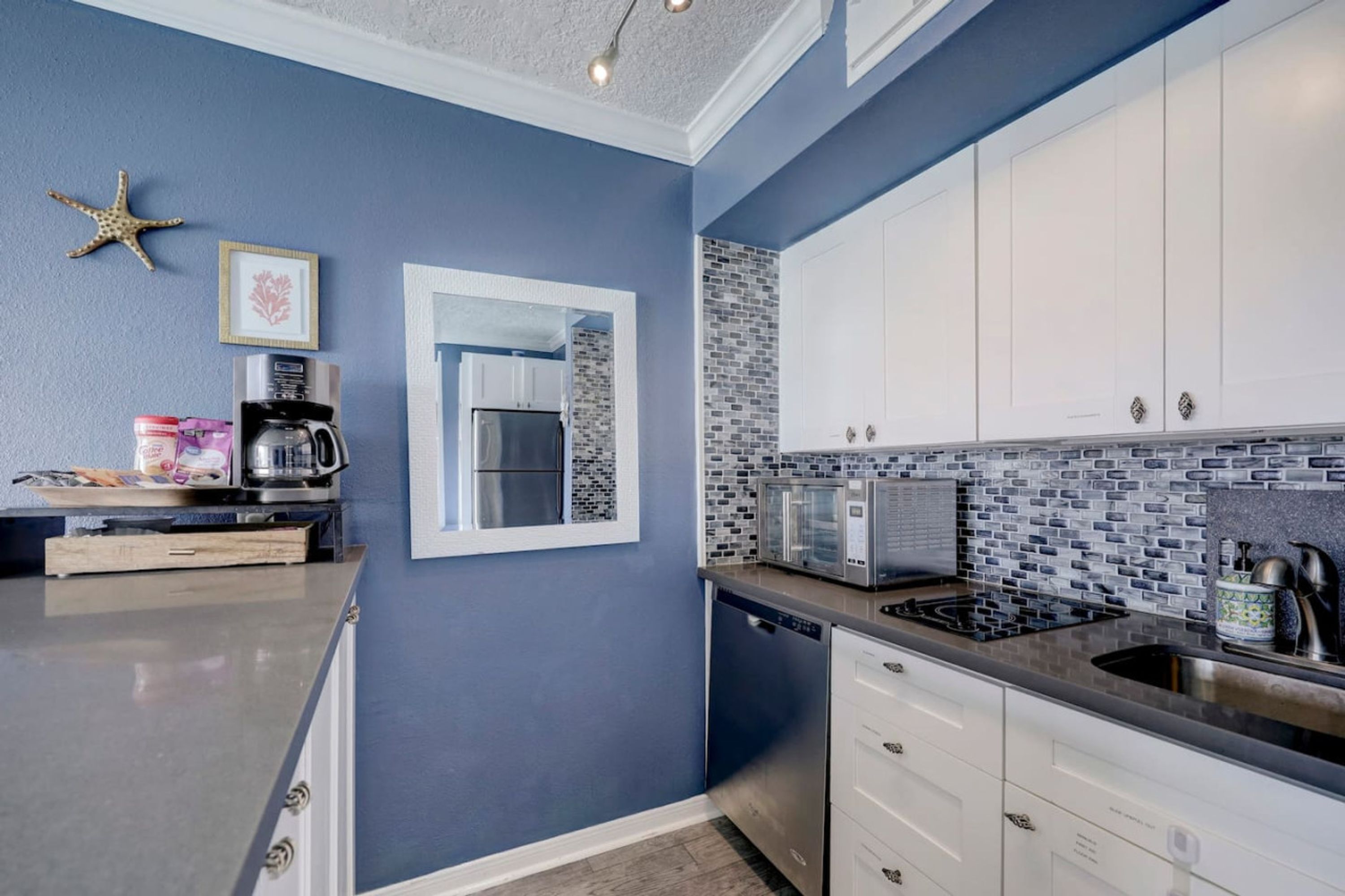 A modern kitchen with blue walls, white cabinets, a tiled backsplash, and stainless steel appliances.