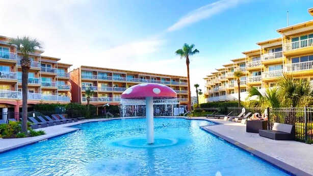 A swimming pool with a mushroom-shaped fountain, surrounded by lounge chairs and palm trees. - Beautiful Ocean Views at The Victorian (Galveston)