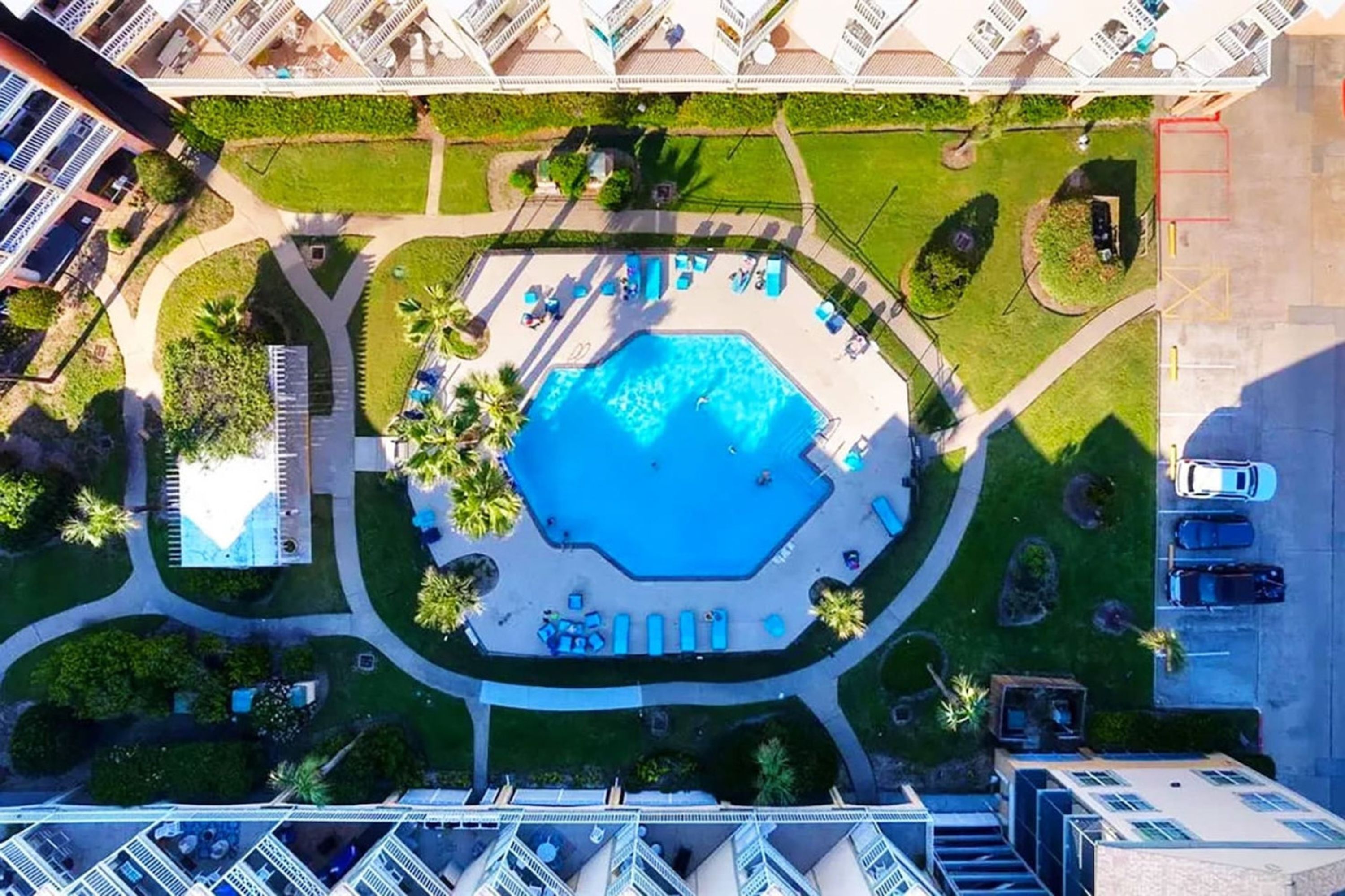 An aerial view of a hotel with a central swimming pool, surrounded by lounge areas and palm trees.