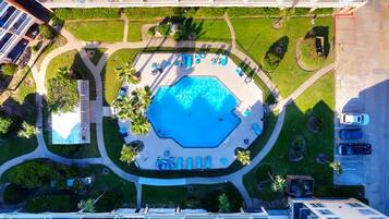An aerial view of a hotel with a central swimming pool, surrounded by lounge areas and palm trees.