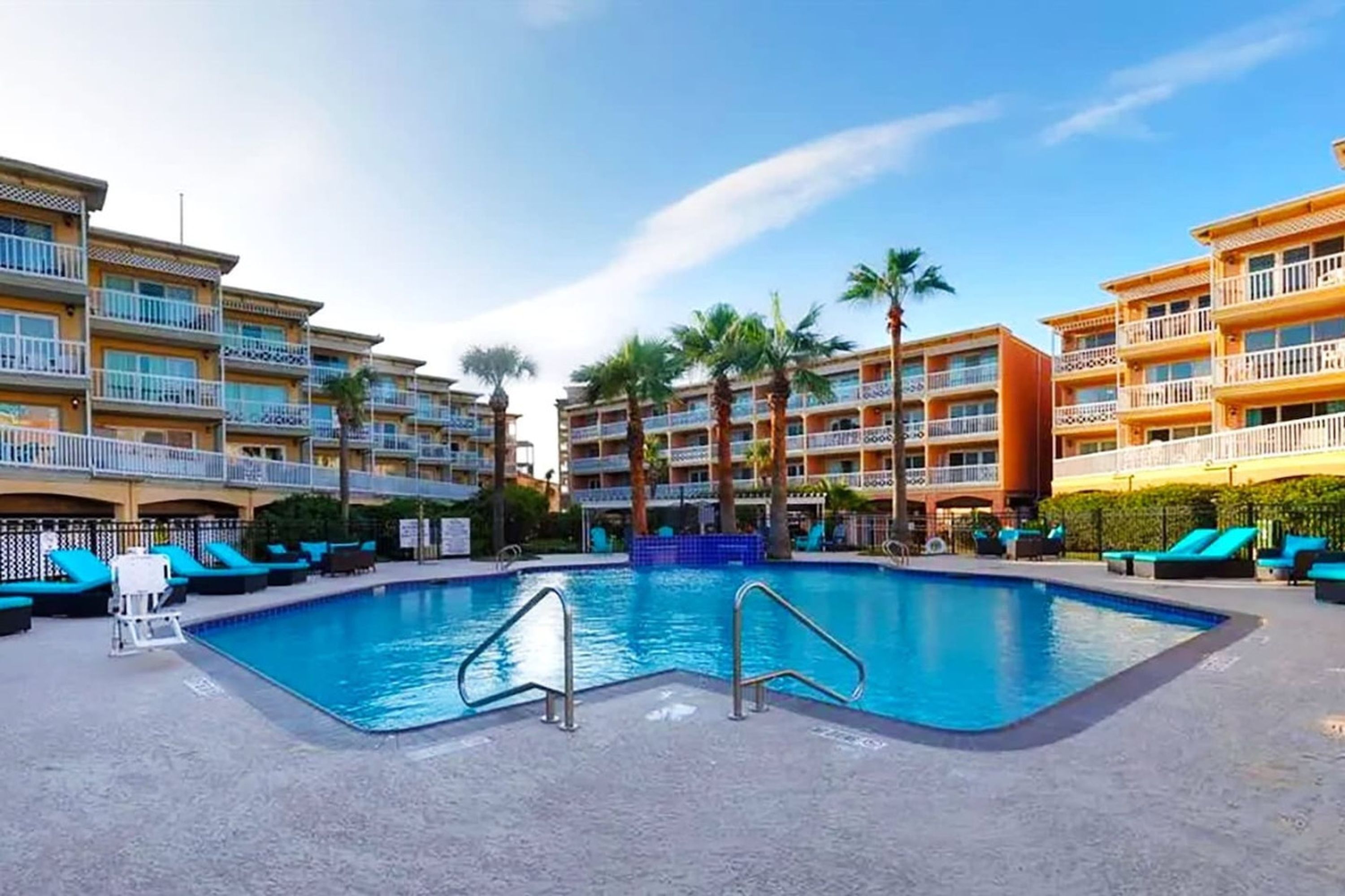 A hotel pool area with multiple balconies, palm trees, and lounge chairs.