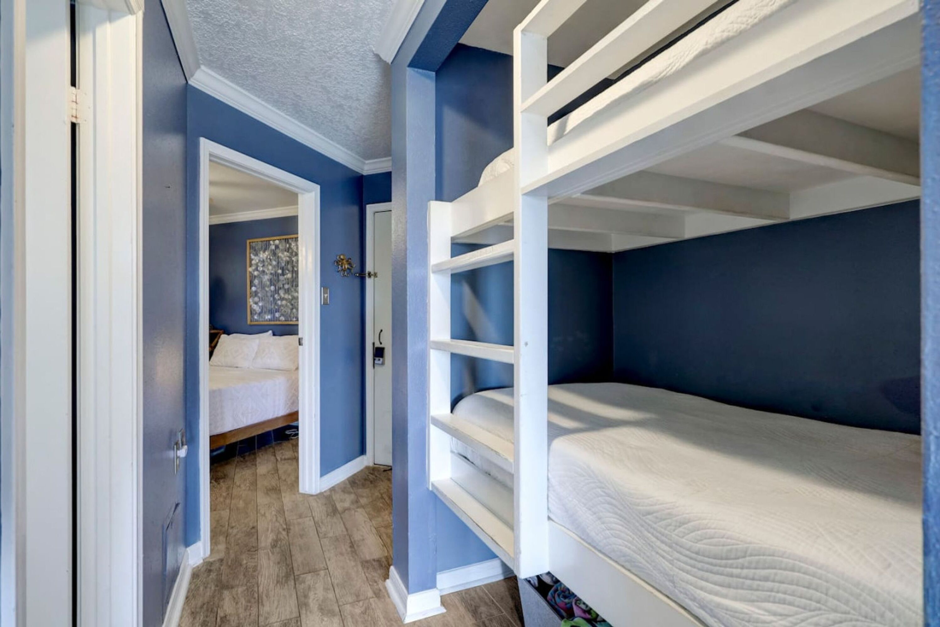 A room with bunk beds, a door leading to another room, and a wooden floor.