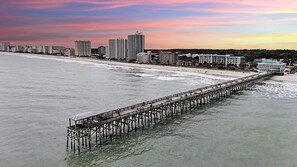 A long pier extending into the water with buildings in the background.