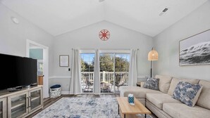 A modern living room with a television, sofa, and a view of the outdoors through large sliding doors. - Wild Iris Condo - Cozy Myrtle Beach Retreat (Myrtle Beach)