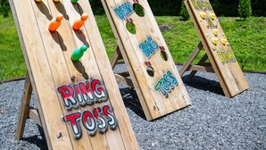 Tre træ ringkastspil med skilte, der viser "RING JOSS", "BØNPOSEKAST" og "FANGER ANDEN."