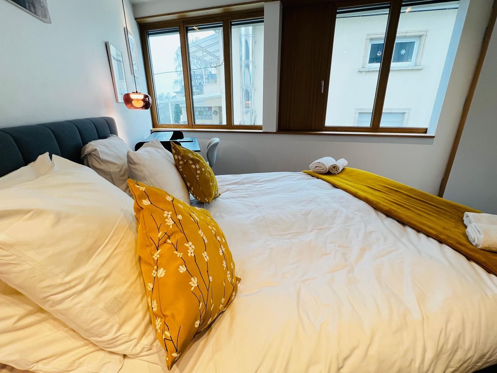 Habitación de hotel con cama, almohadas, escritorio y ventana con vistas a edificios.